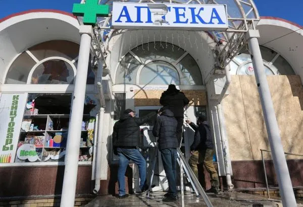 Мужчины ремонтируют здание аптеки, поврежденное в результате обстрела ВСУ рынка в Кировском районе Донецка.